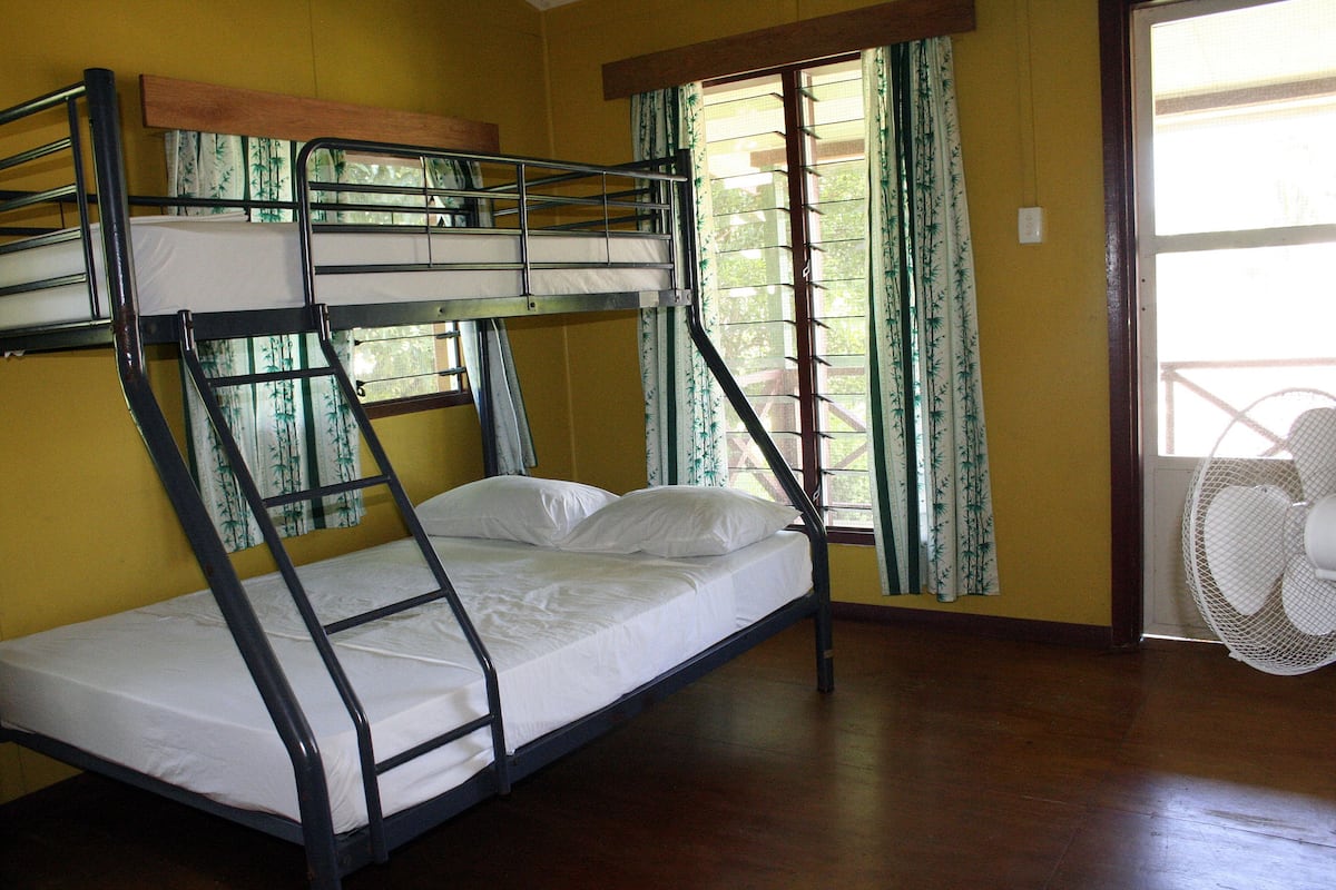 A bunk bed room with a window and a standing fan.