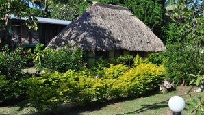 A thatched-roof hut surrounded by lush greenery and a well-maintained garden. - Ratu Kini Backpackers & Dive Resort (Mana Island)