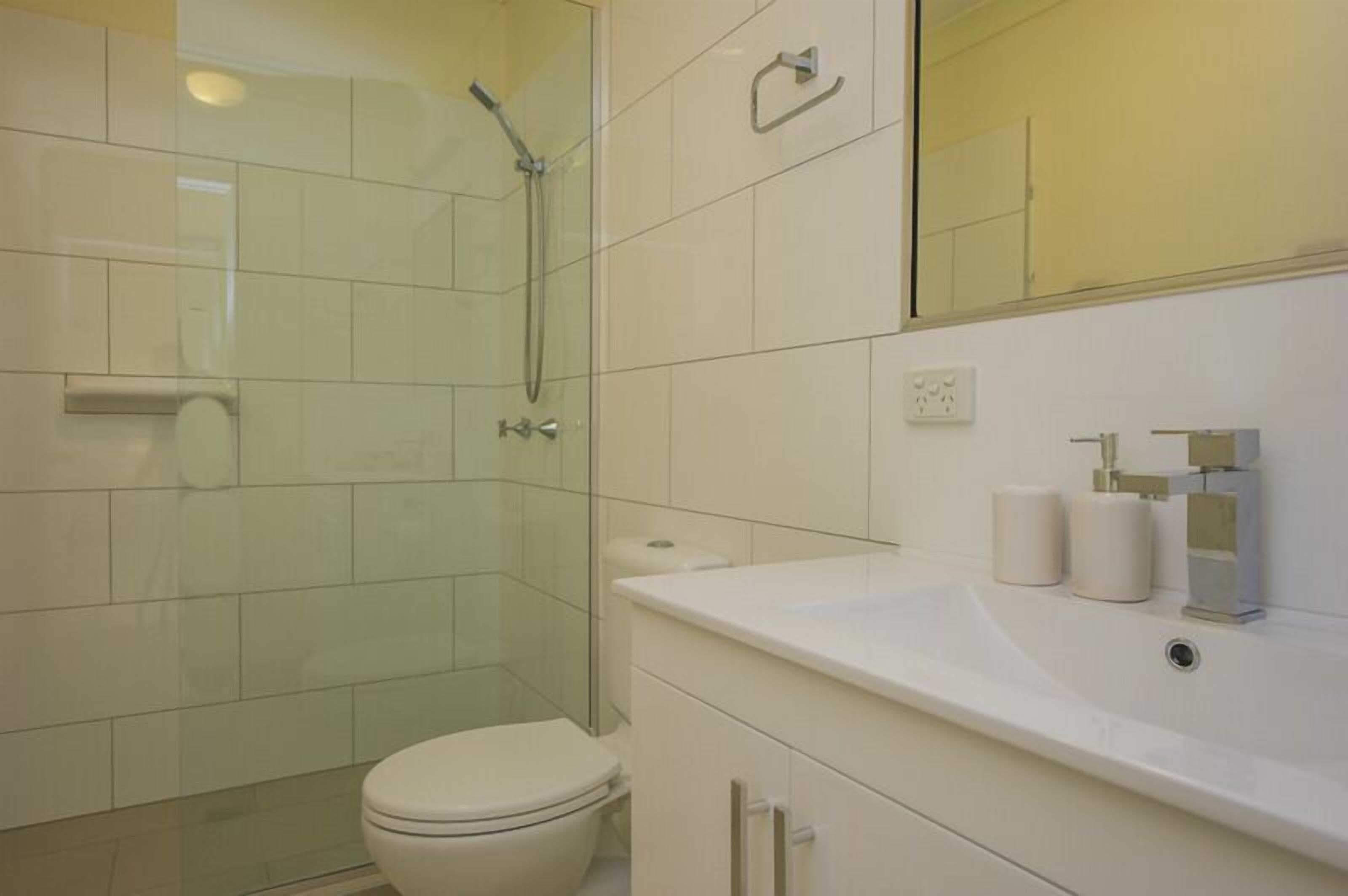 Un baño moderno con cabina de ducha de vidrio, inodoro blanco y tocador con lavamanos y espejo.