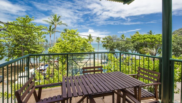 A wooden table and bench on a balcony with a view of palm trees and a clear sky. - Magnetic Sunsets Resort (Horseshoe Bay)