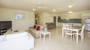 A modern living room with a sofa, coffee table, and TV, a dining area with a table and chairs, and a kitchen with cabinets and appliances. - Magnetic Sunsets Resort (Horseshoe Bay)