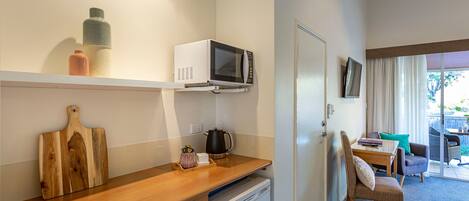 A compact kitchen with a microwave, kettle, and wooden cutting board.