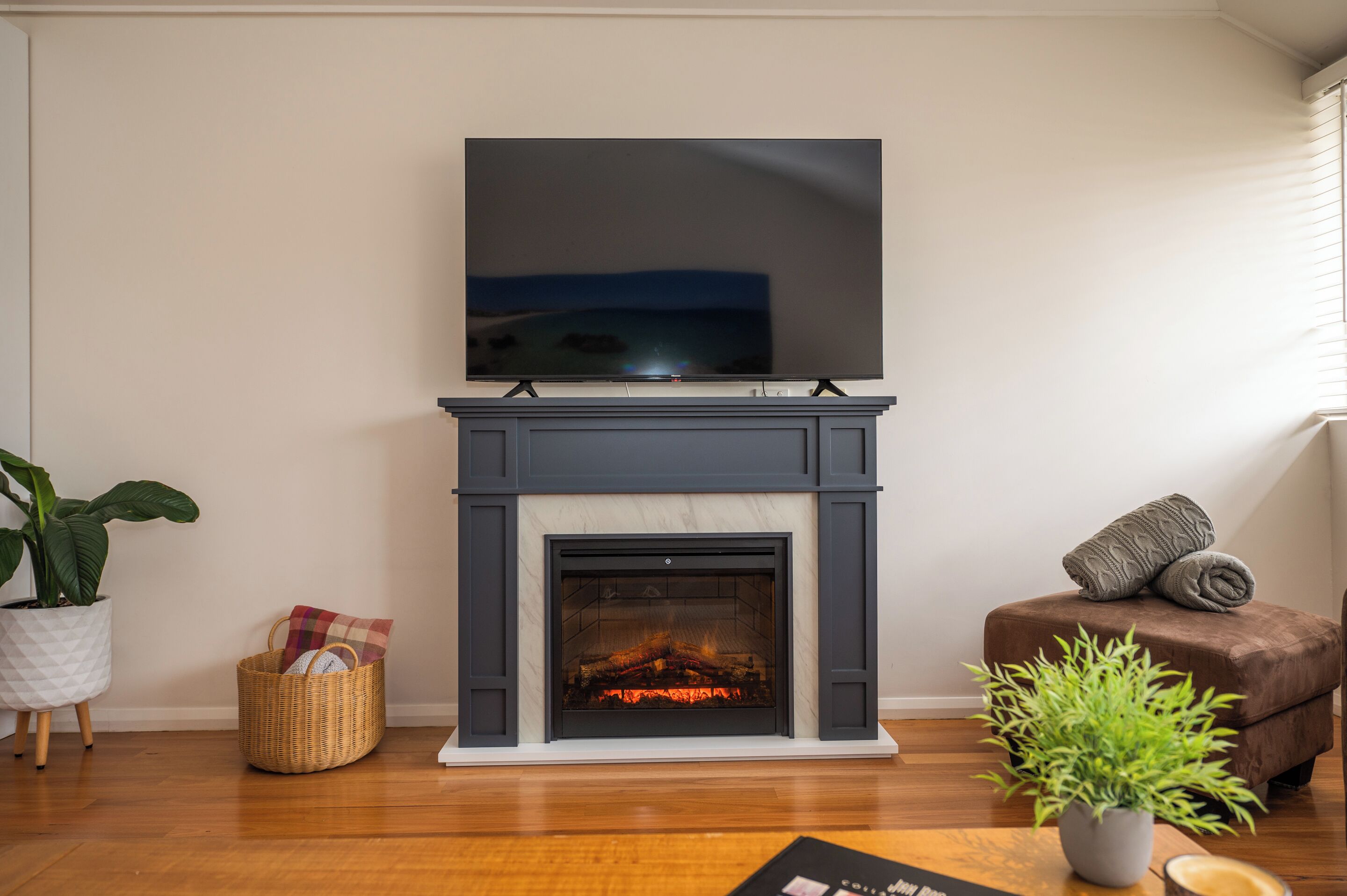 A living room with a fireplace, a flat-screen TV mounted above it, a brown sofa, and a potted plant.