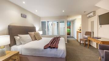 Quarto de hotel com uma cama grande, uma escrivaninha, uma cadeira e uma televisão.