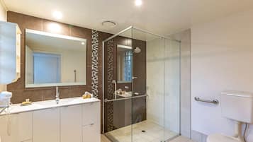 A modern bathroom with a glass-enclosed shower, a large mirror, and a white toilet.