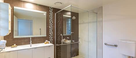 A modern bathroom with a glass-enclosed shower, a large mirror, and a white toilet.