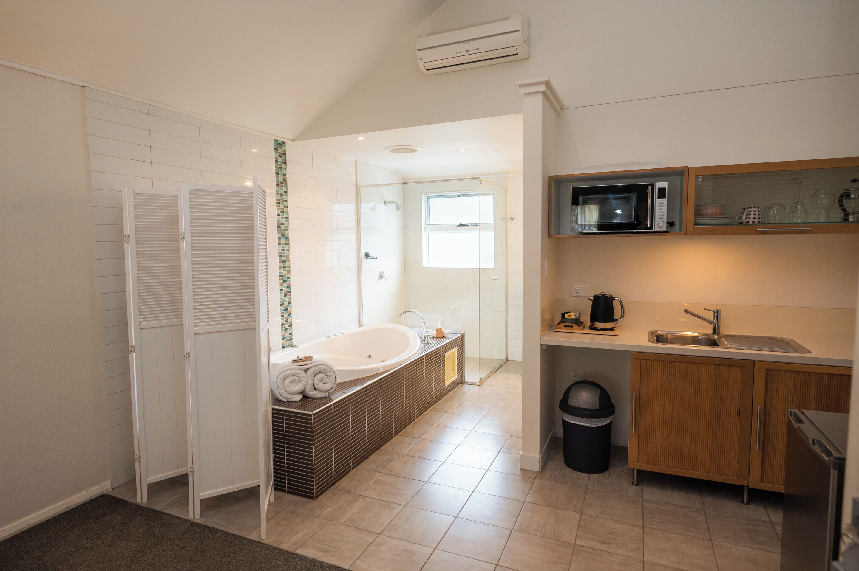 Een moderne badkamer met een vrijstaand bad, een douchegedeelte en een keuken met een magnetron en spoelbak.