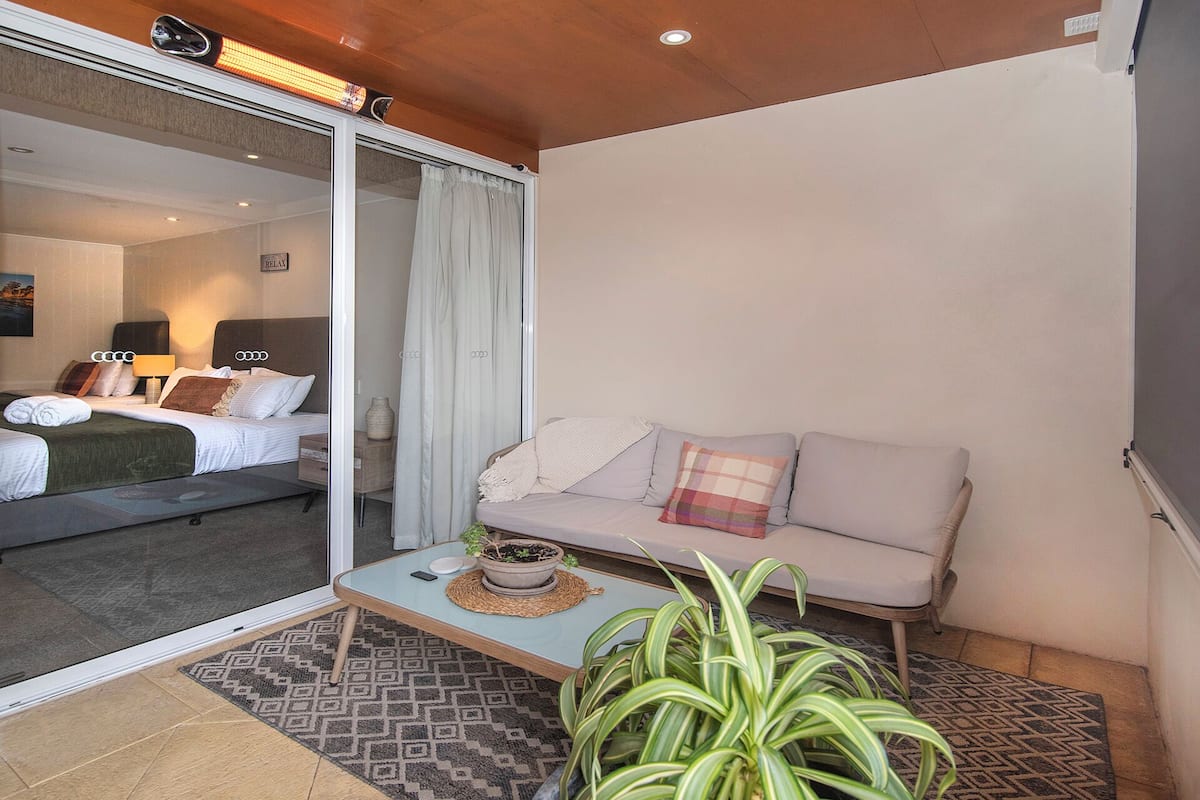 Una habitación de hotel moderna con una cama, un sofá, una mesita con una planta y un ventanal corredero que da a un balcón.