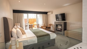 Una habitación de hotel moderna con una cama grande, un jacuzzi con cerramiento de vidrio, un televisor de pantalla plana y una zona de comedor con mobiliario de mimbre.