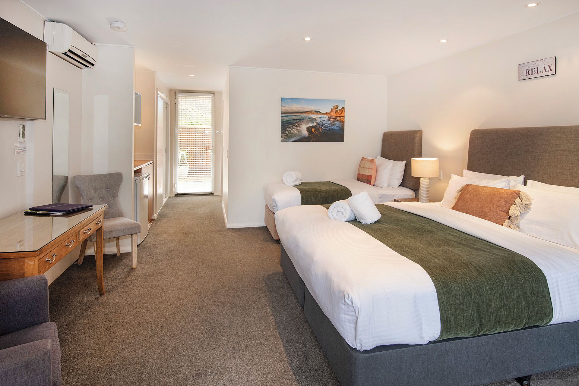 A hotel room with two beds, a desk, a chair, a TV, and a painting on the wall.