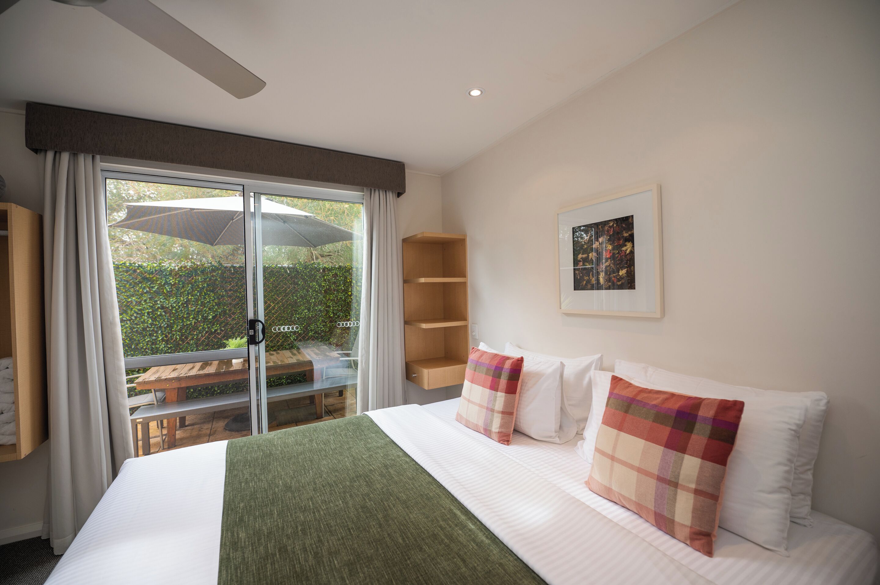 A hotel room with a large bed, a view of the outdoors, a wooden bench outside, and a ceiling fan.