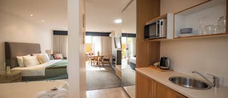 A modern hotel room with a large bed, a bathroom with a bathtub, a kitchenette, and a dining area.