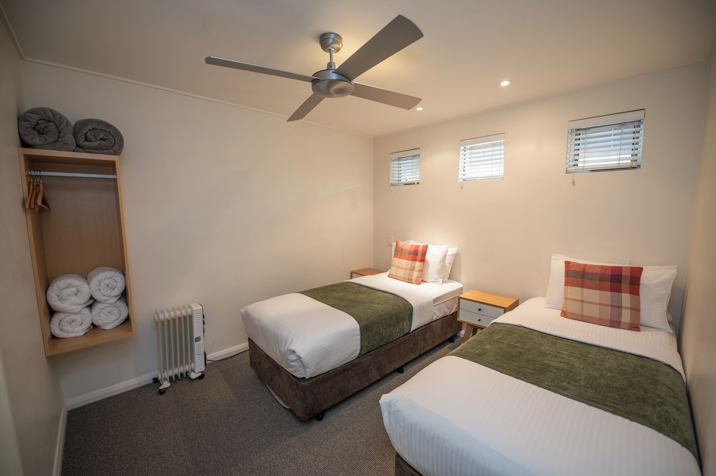 Habitación de hotel con dos camas, un ventilador de techo, un radiador y una estantería con toallas.
