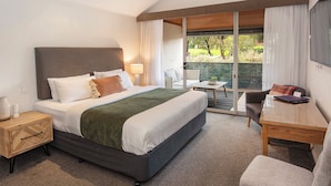 Habitación de hotel moderna con una cama grande, un escritorio y un balcón con vistas a zonas verdes.