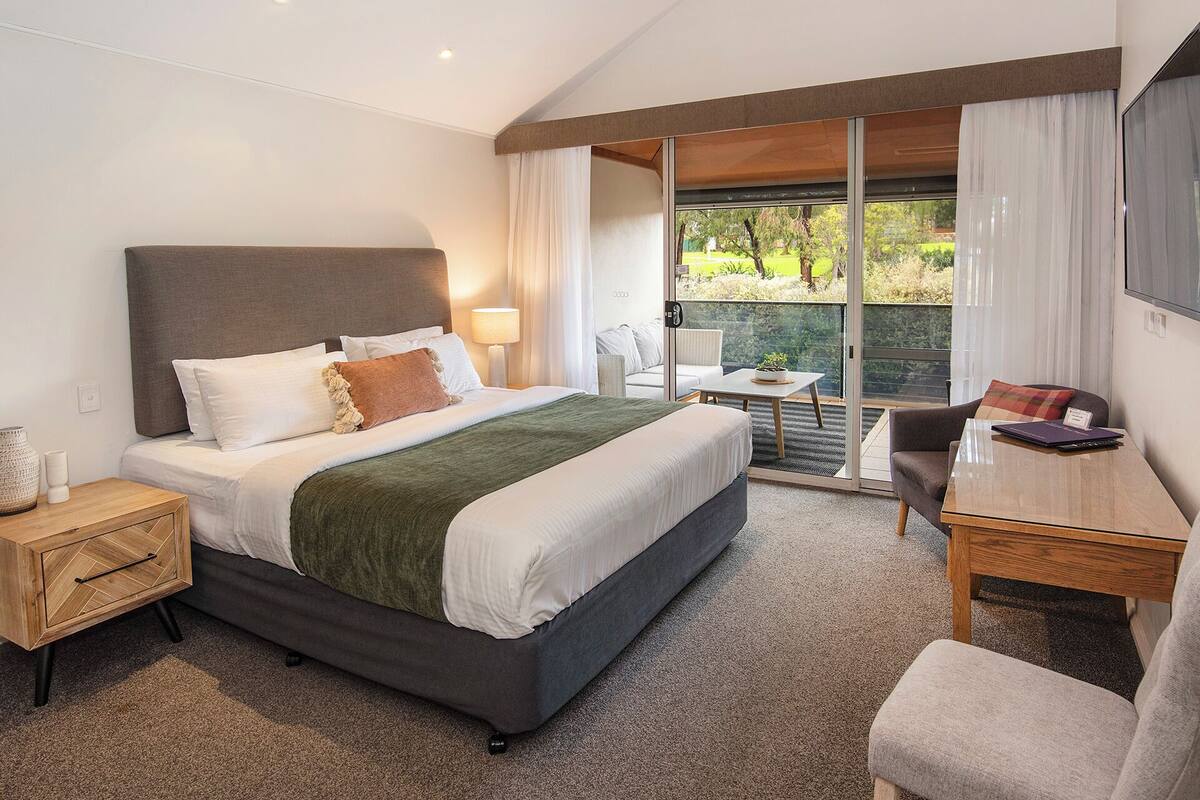 Habitación de hotel moderna con una cama grande, un escritorio y un balcón con vistas a zonas verdes.