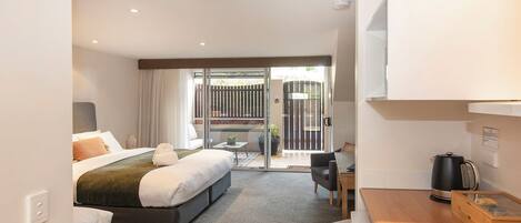 A hotel room with a bed, a small desk, a chair, a coffee maker, and a sliding glass door leading to a balcony.