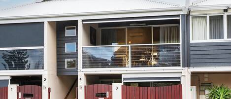A row of townhouses with a central staircase, numbered doors, and a balcony with a view.