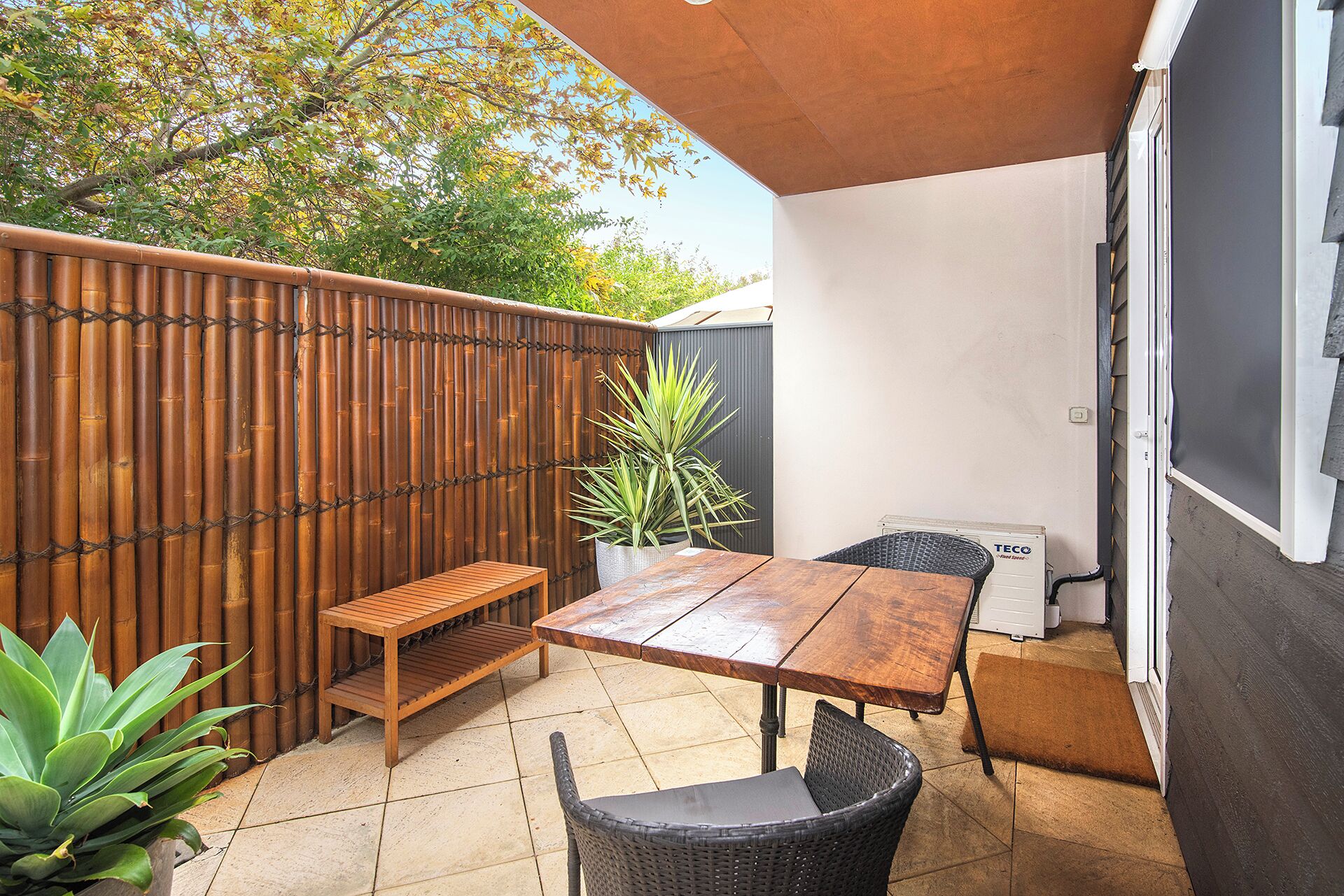 Un patio al aire libre con una mesa y sillas de madera, una cerca de bambú y una planta en maceta.