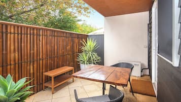 Un patio al aire libre con una mesa y sillas de madera, una cerca de bambú y una planta en maceta.