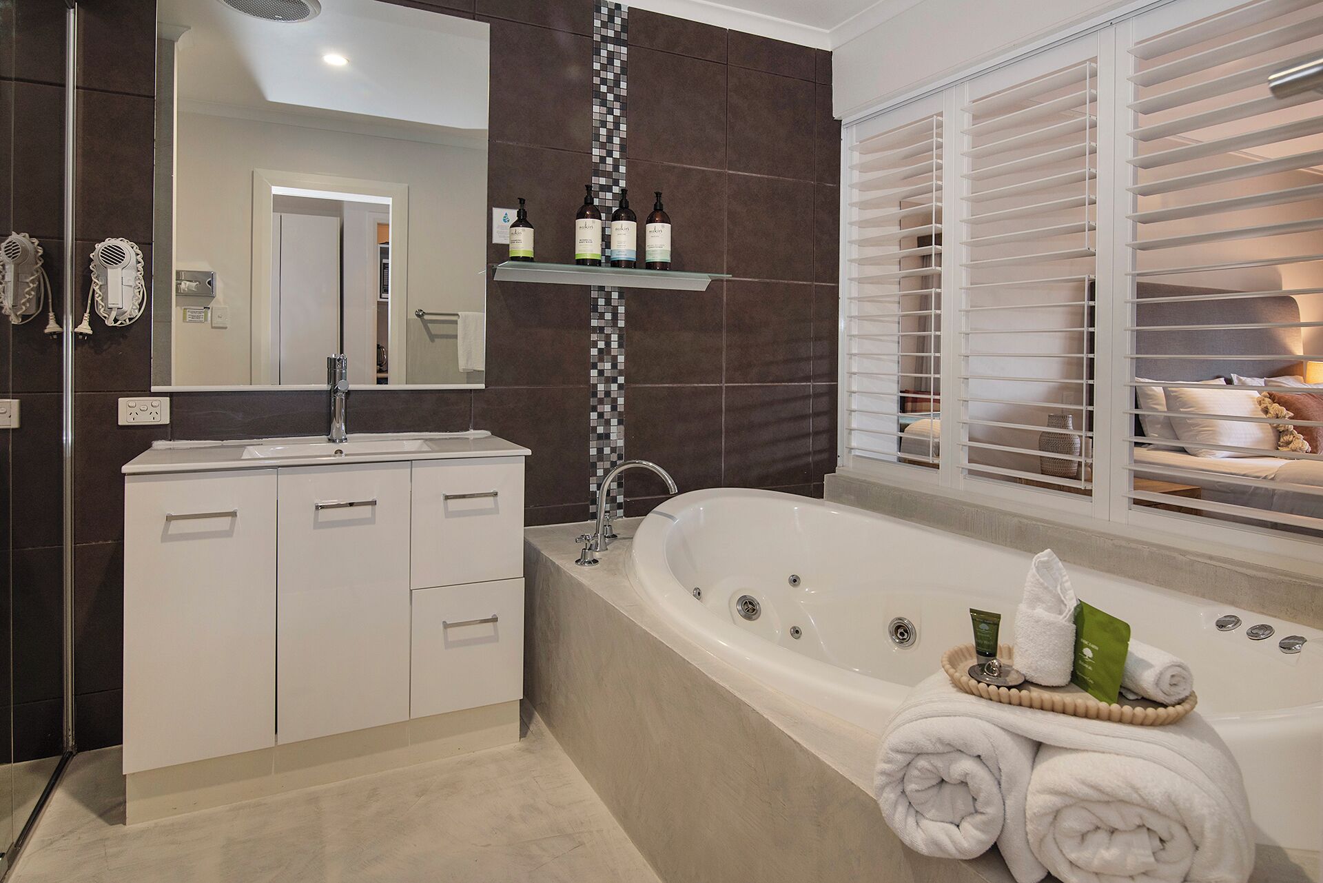 A modern bathroom with a freestanding bathtub, a vanity with a mirror, and a shelf with toiletries.