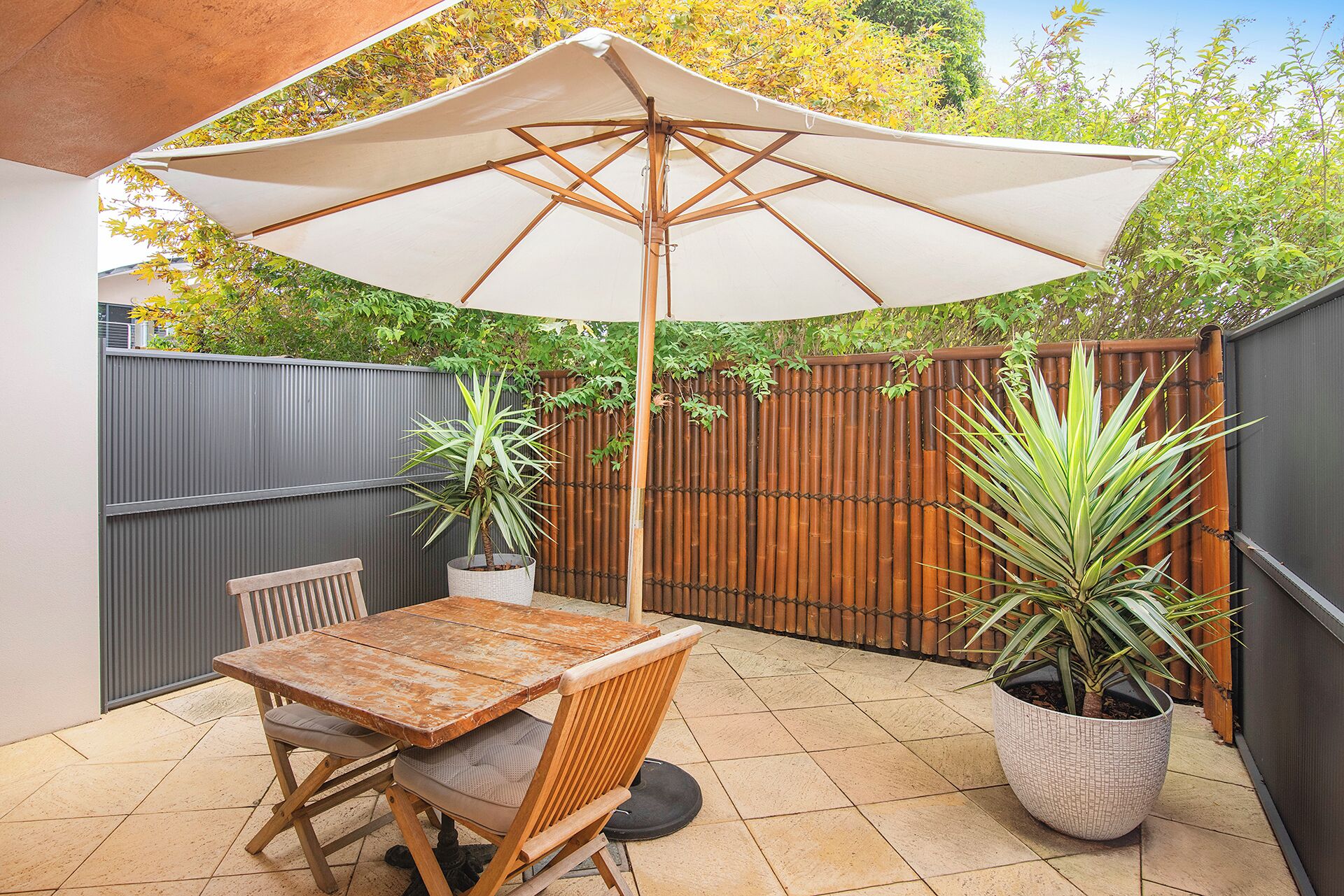 Une terrasse avec une table et des chaises en bois, un grand parasol et des plantes en pot.