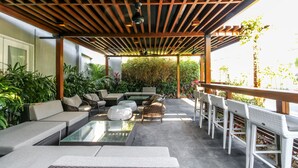 Une terrasse extérieure agrémentée d’une pergola en bois, de coins salon et d’une végétation luxuriante.