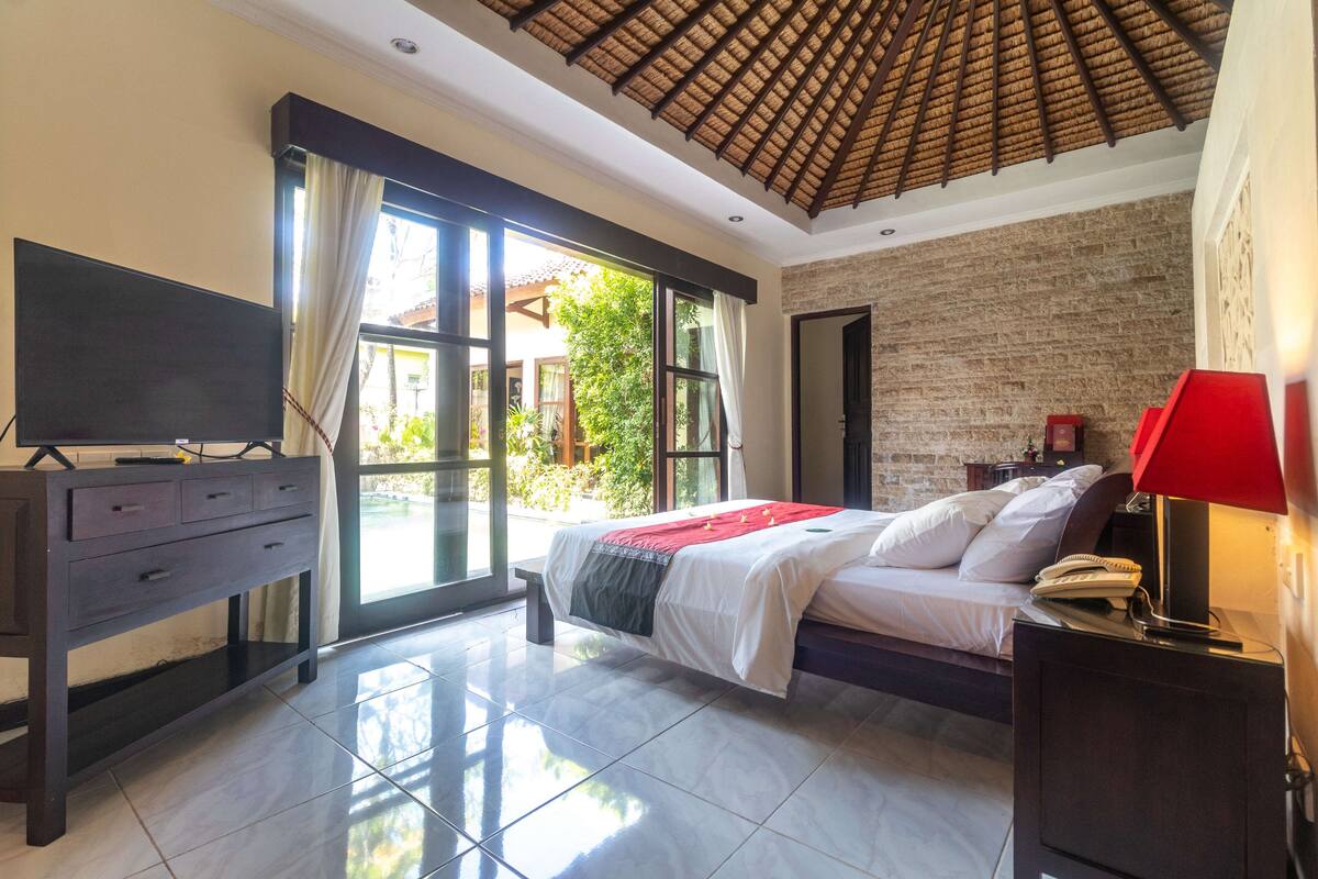 A bedroom with a bed, a TV, a desk, and a window with curtains.