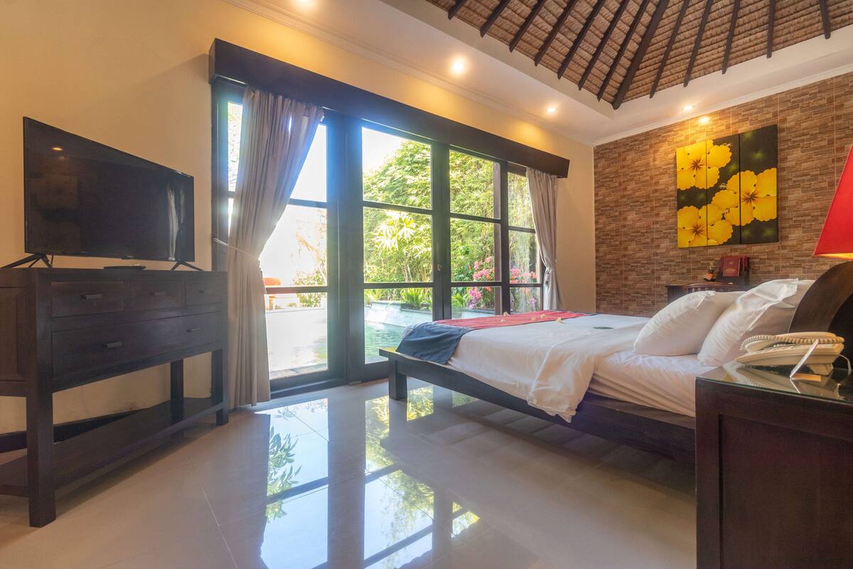 A bedroom with a bed, a TV, a desk, and a window with curtains.