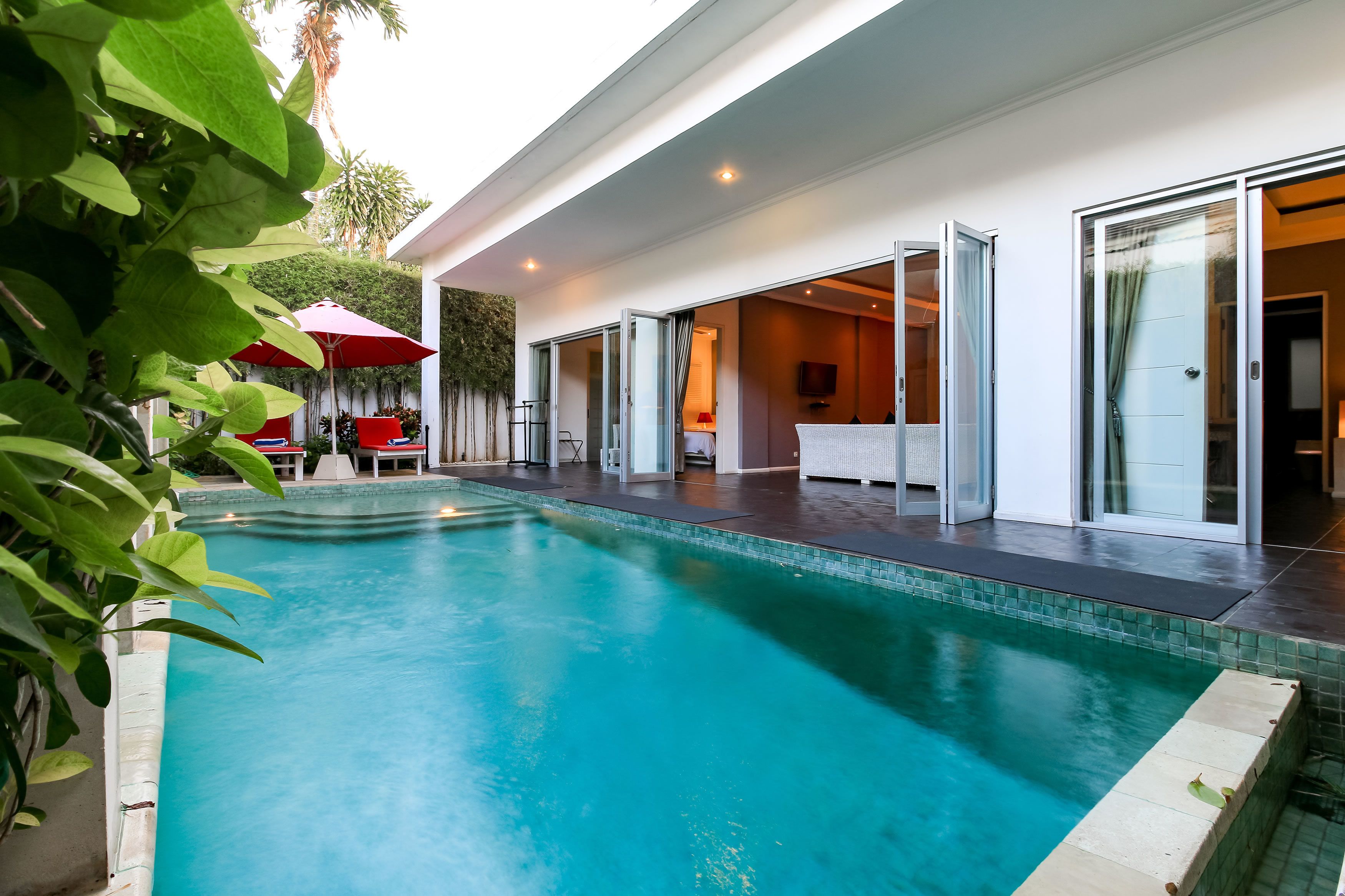 A modern pool area with a clear blue pool, a red umbrella, and a glass door entrance.