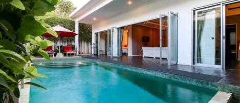 A modern pool area with a clear blue pool, a red umbrella, and a glass door entrance.