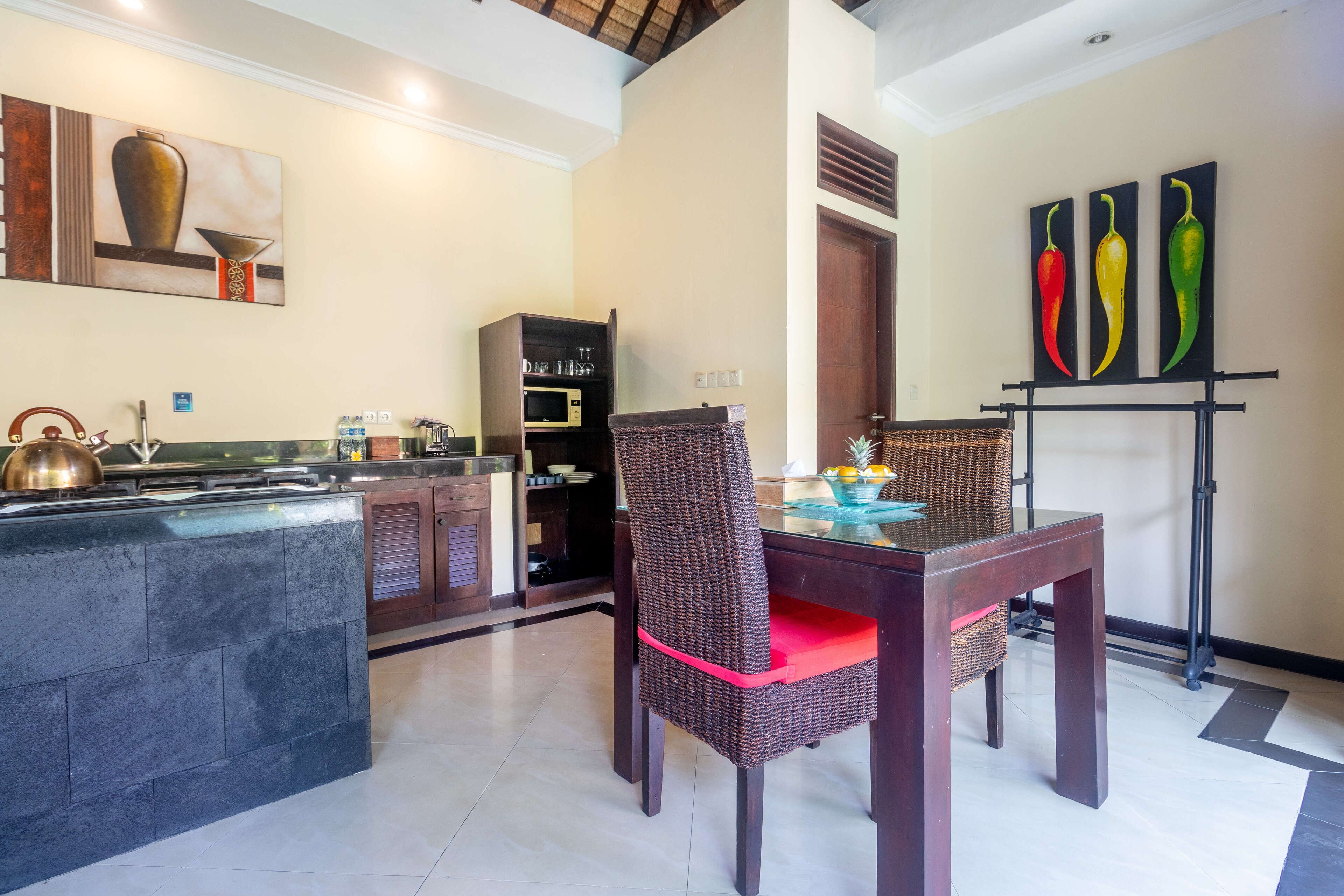 A modern kitchen with a central island, dark wooden chairs with red cushions, and a dining table.