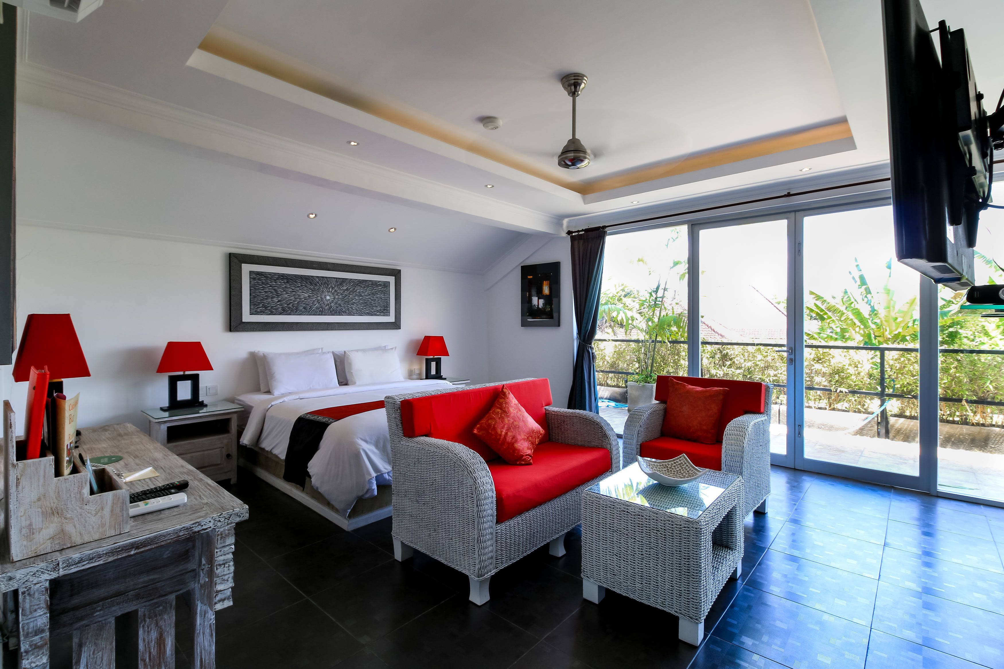 A hotel room with a bed, a red sofa, a small table, and a desk with a lamp.