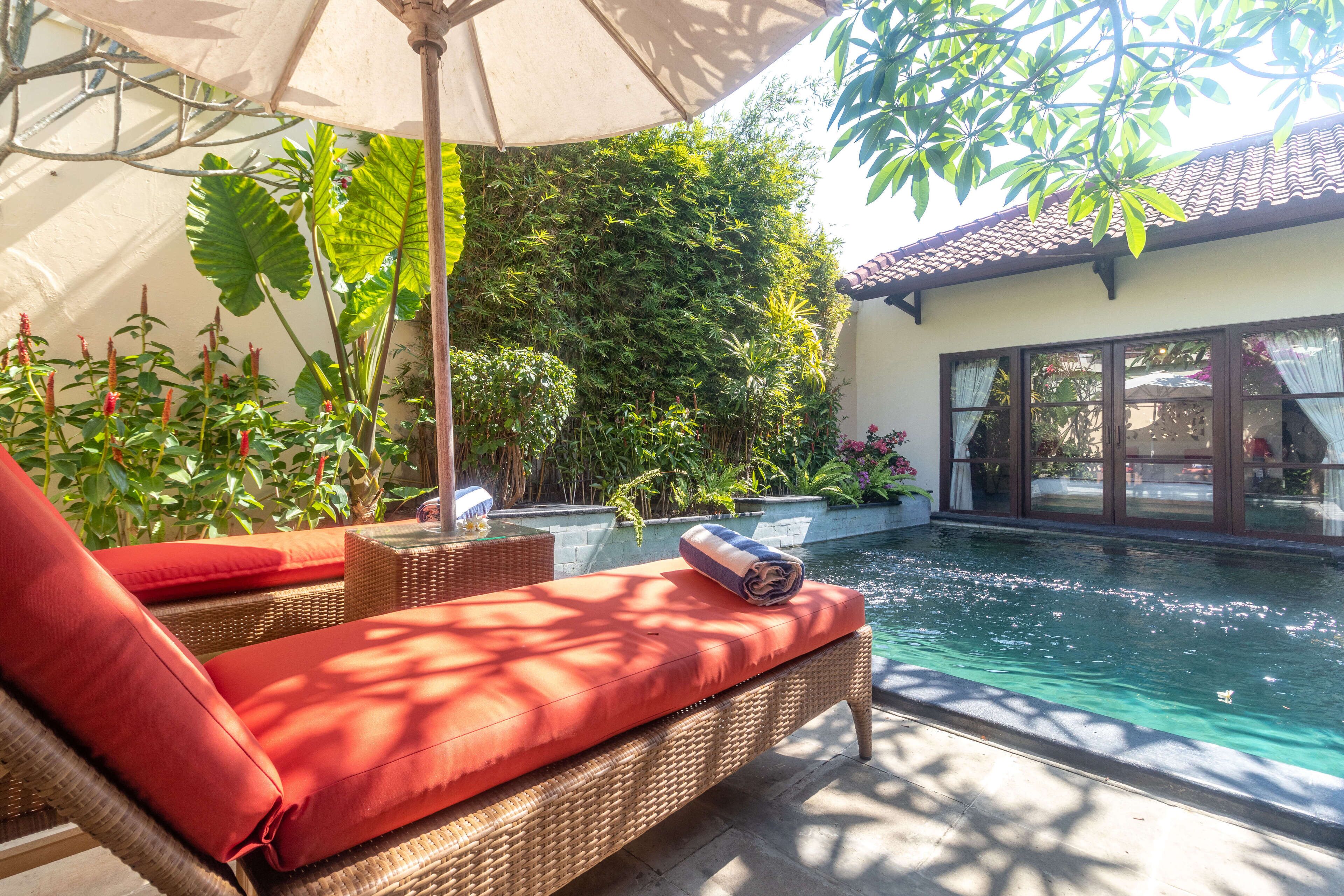 A poolside area with wicker lounge chairs, a small table, and an umbrella.