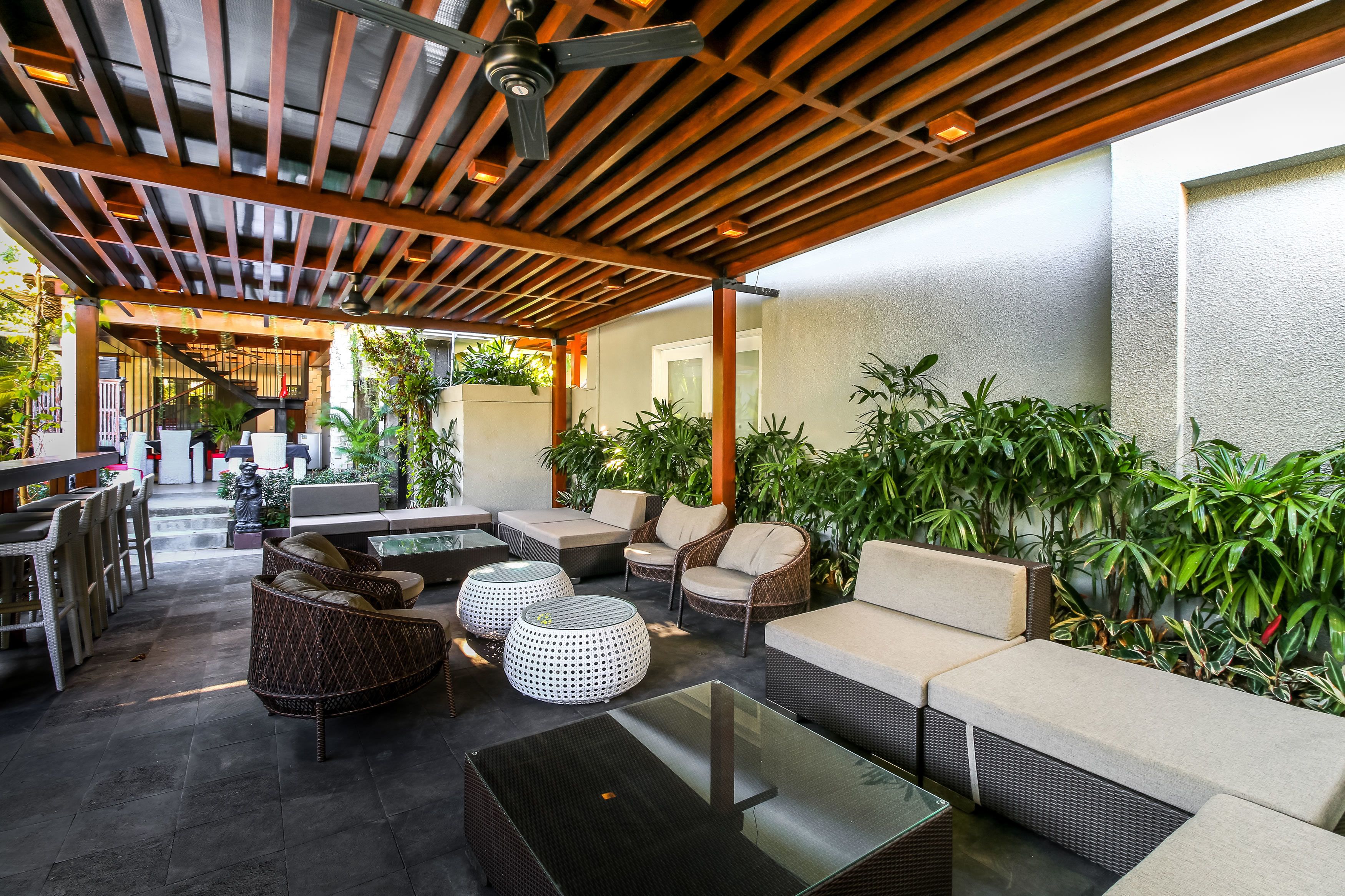 Un espace extérieur aménagé en terrasse, avec des meubles en osier, une table en verre et des plantes en pot.