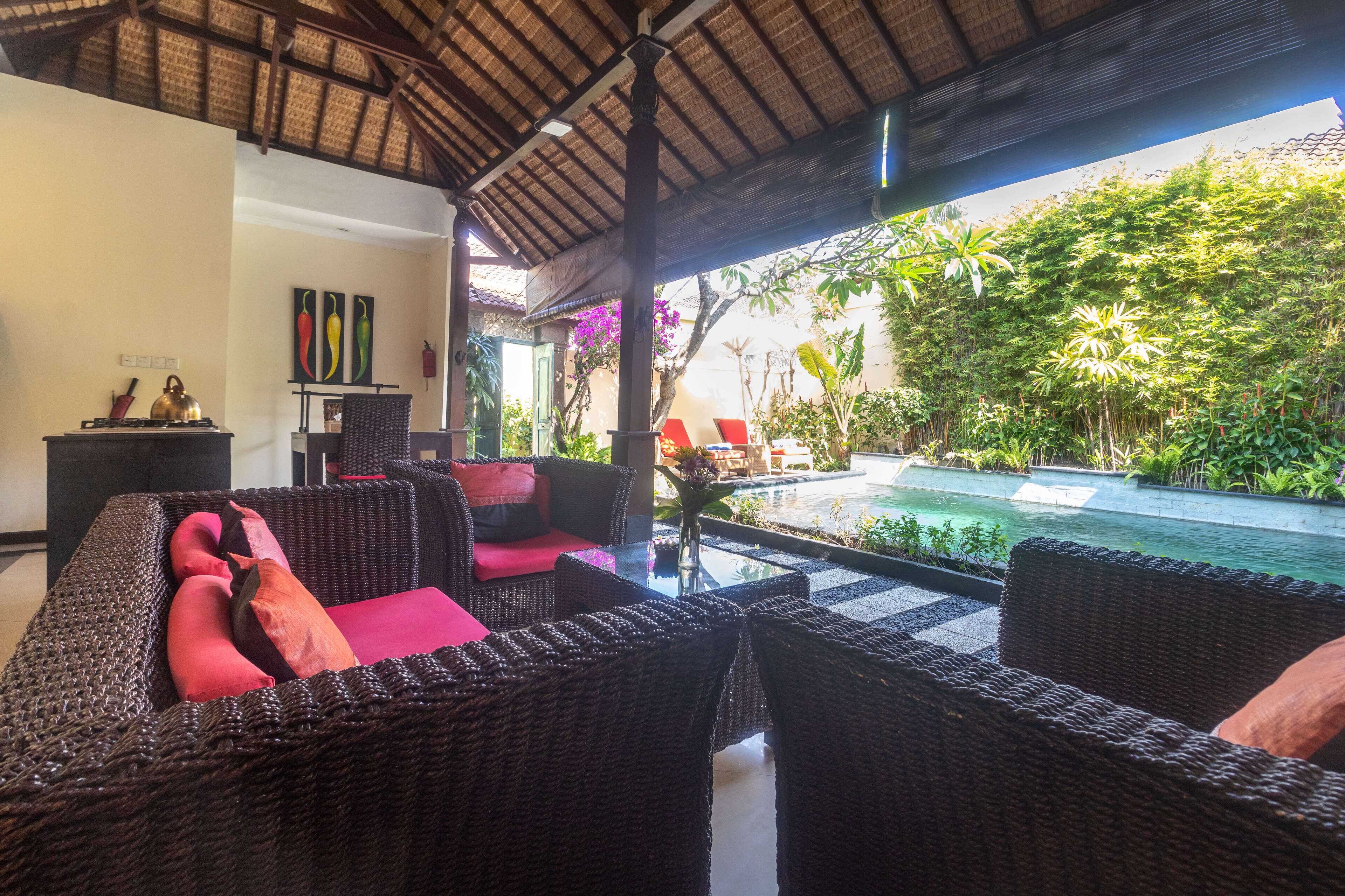 A cozy outdoor seating area with wicker furniture and a view of a swimming pool surrounded by lush greenery.