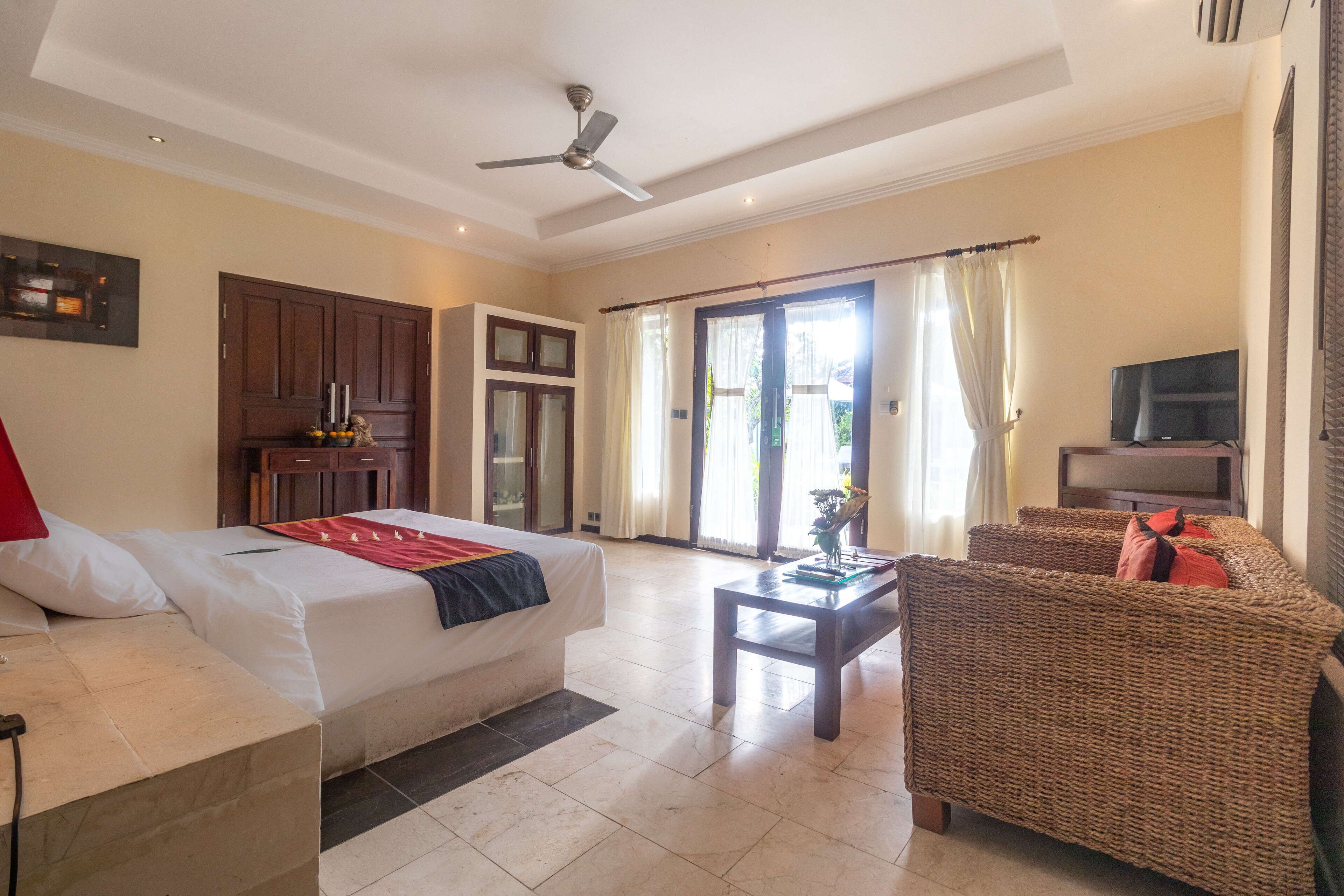 A hotel room with a bed, a sofa, a TV, and a ceiling fan.