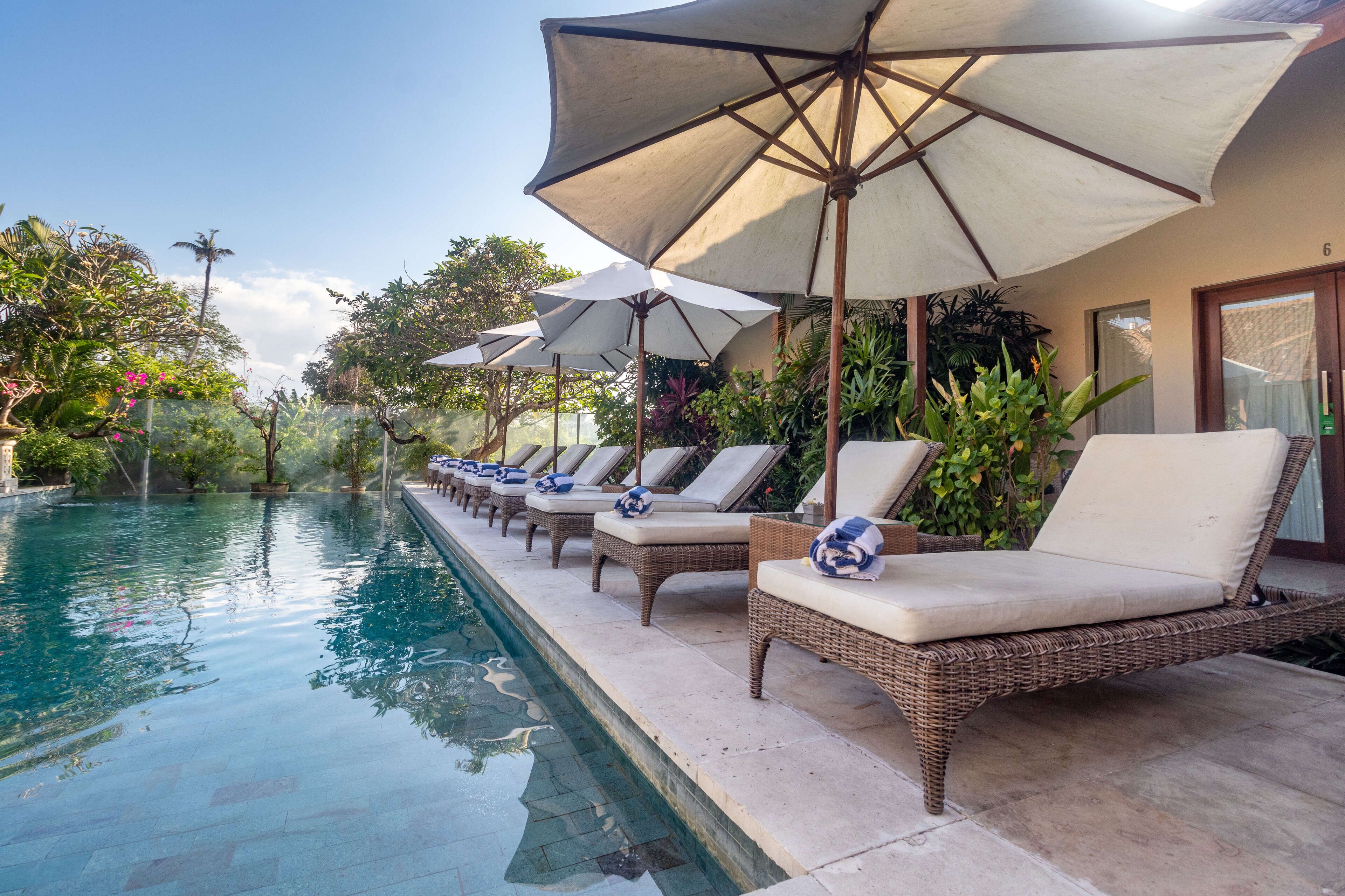 Un espace aménagé au bord de la piscine, avec des chaises longues et des parasols, entouré d’une végétation luxuriante.