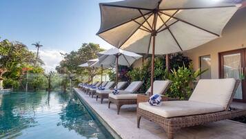 Un espace aménagé au bord de la piscine, avec des chaises longues et des parasols, entouré d’une végétation luxuriante.
