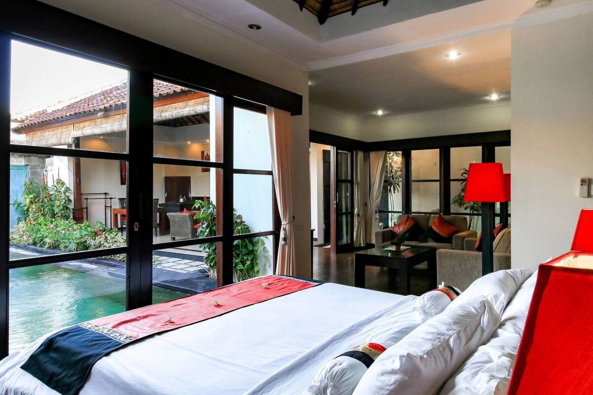 A hotel room with a large bed, a dining area, and a view of a swimming pool.