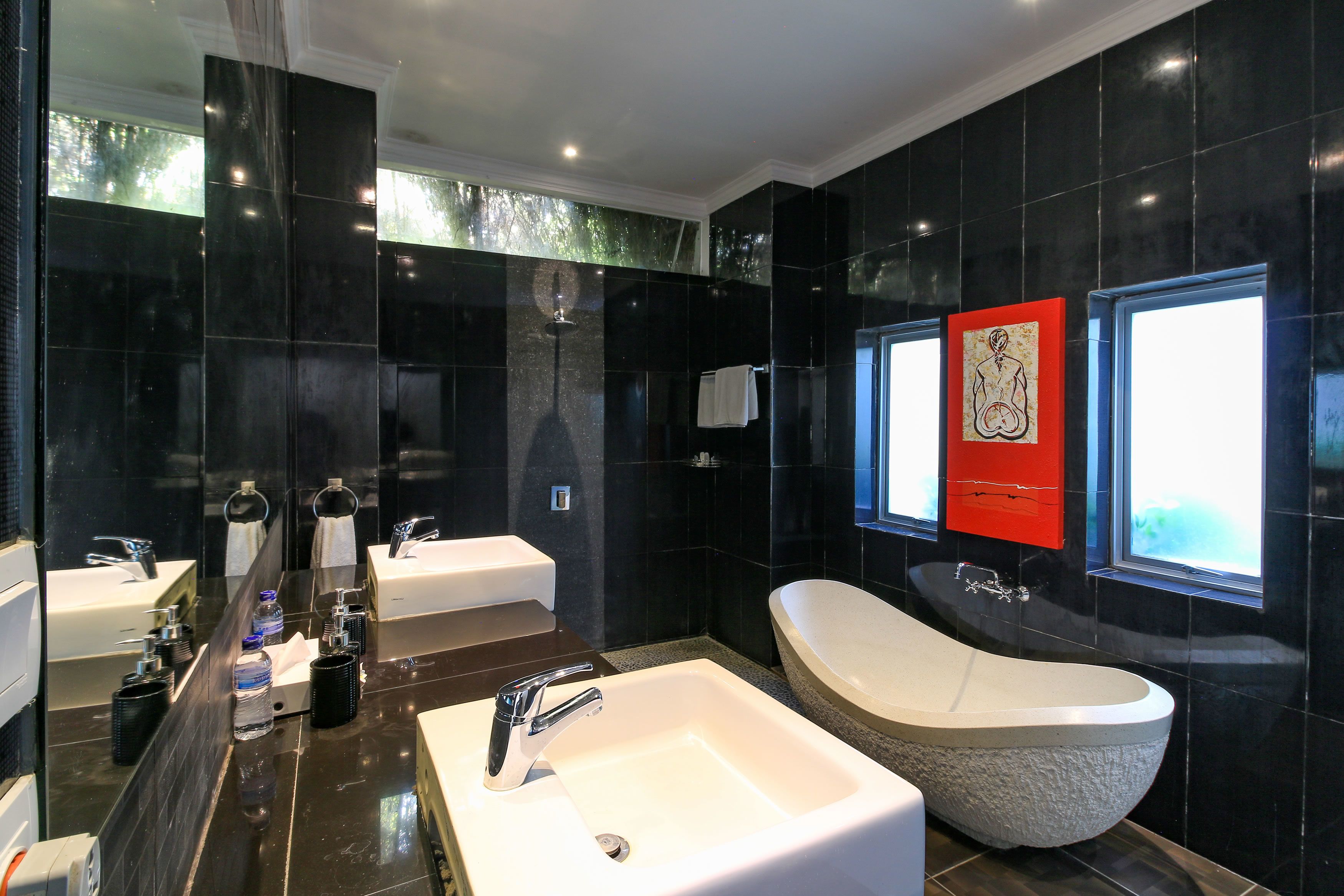 Un baño moderno con un espejo grande, dos lavabos, una bañera y una obra de arte roja en la pared.