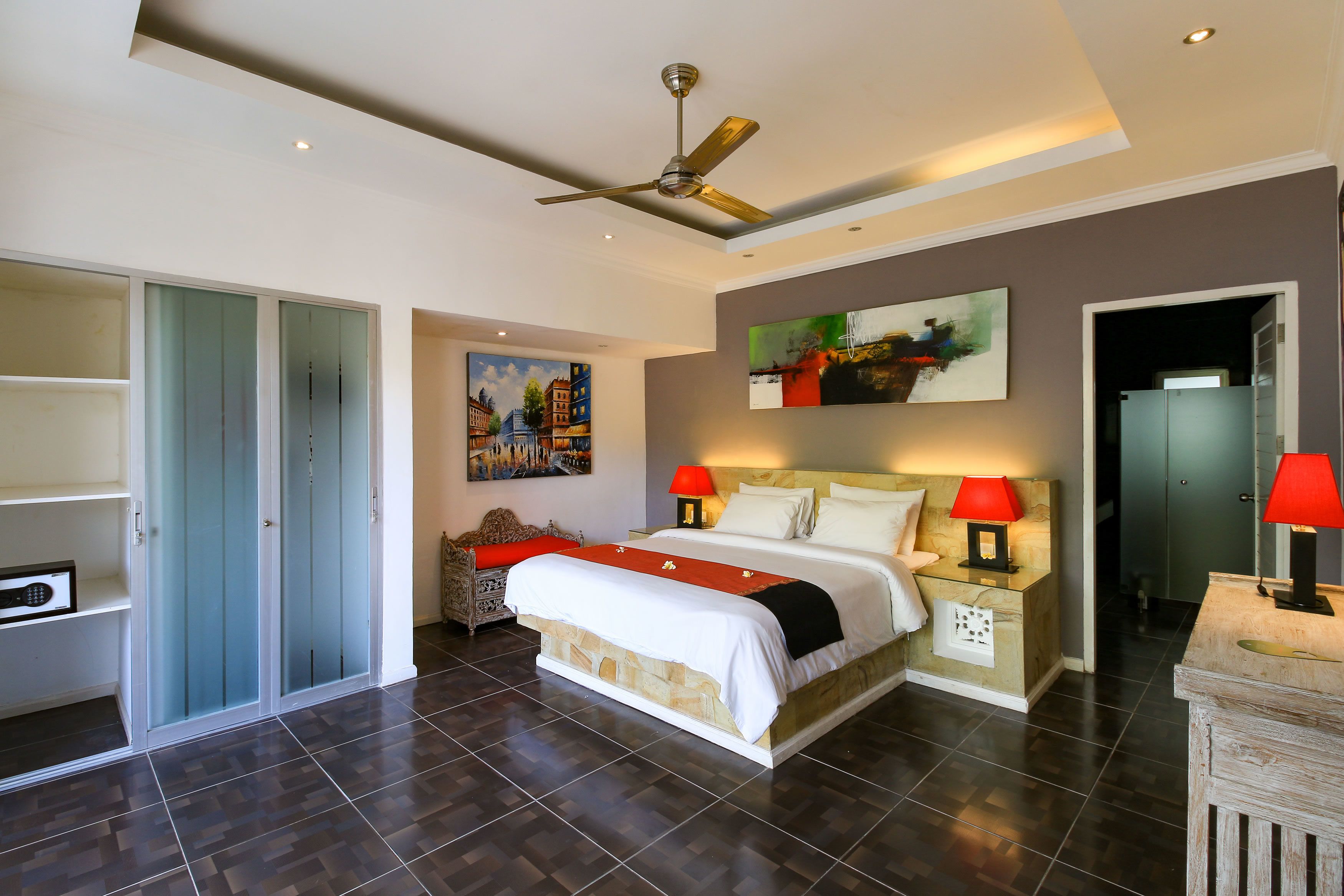 Une chambre d’hôtel avec un grand lit, deux lampes de chevet, un ventilateur de plafond et des œuvres d’art accrochées aux murs.