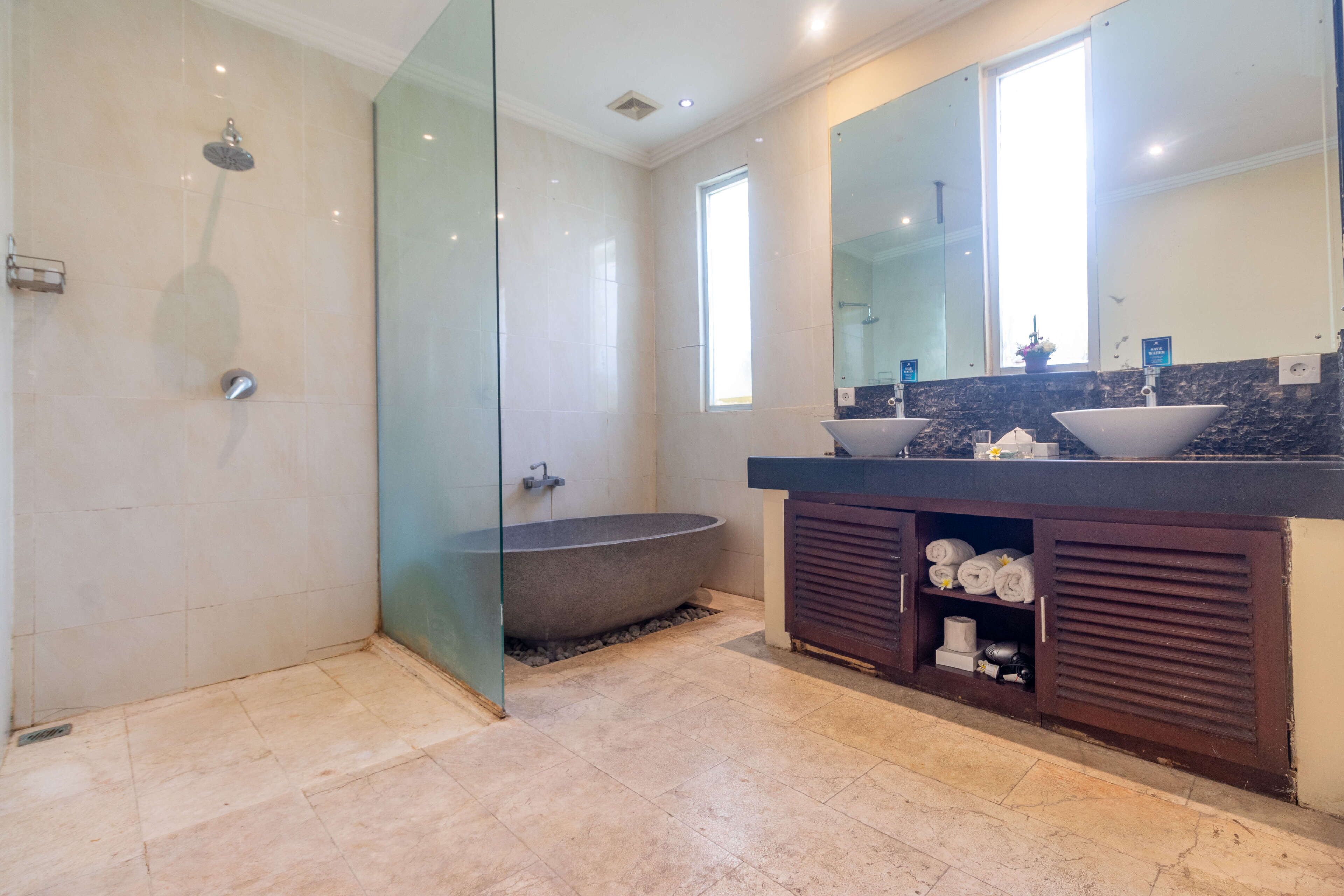 Un baño moderno con ducha envuelta en vidrio, una bañera independiente y un lavamanos con un espejo grande y dos lavabos.