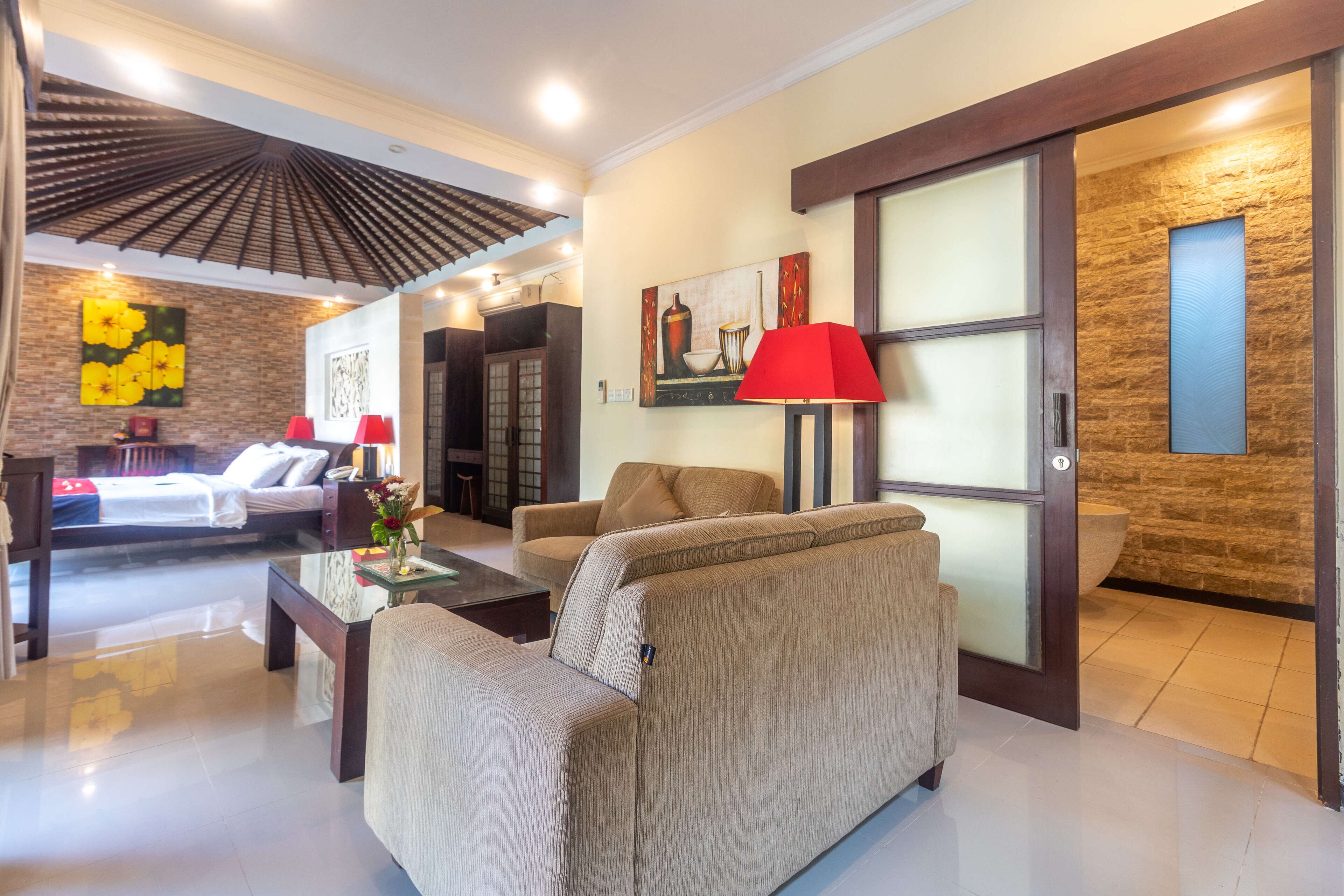 A modern living room with a sofa, a coffee table, and a red lamp. There is a painting on the wall and a wooden door with a glass panel.