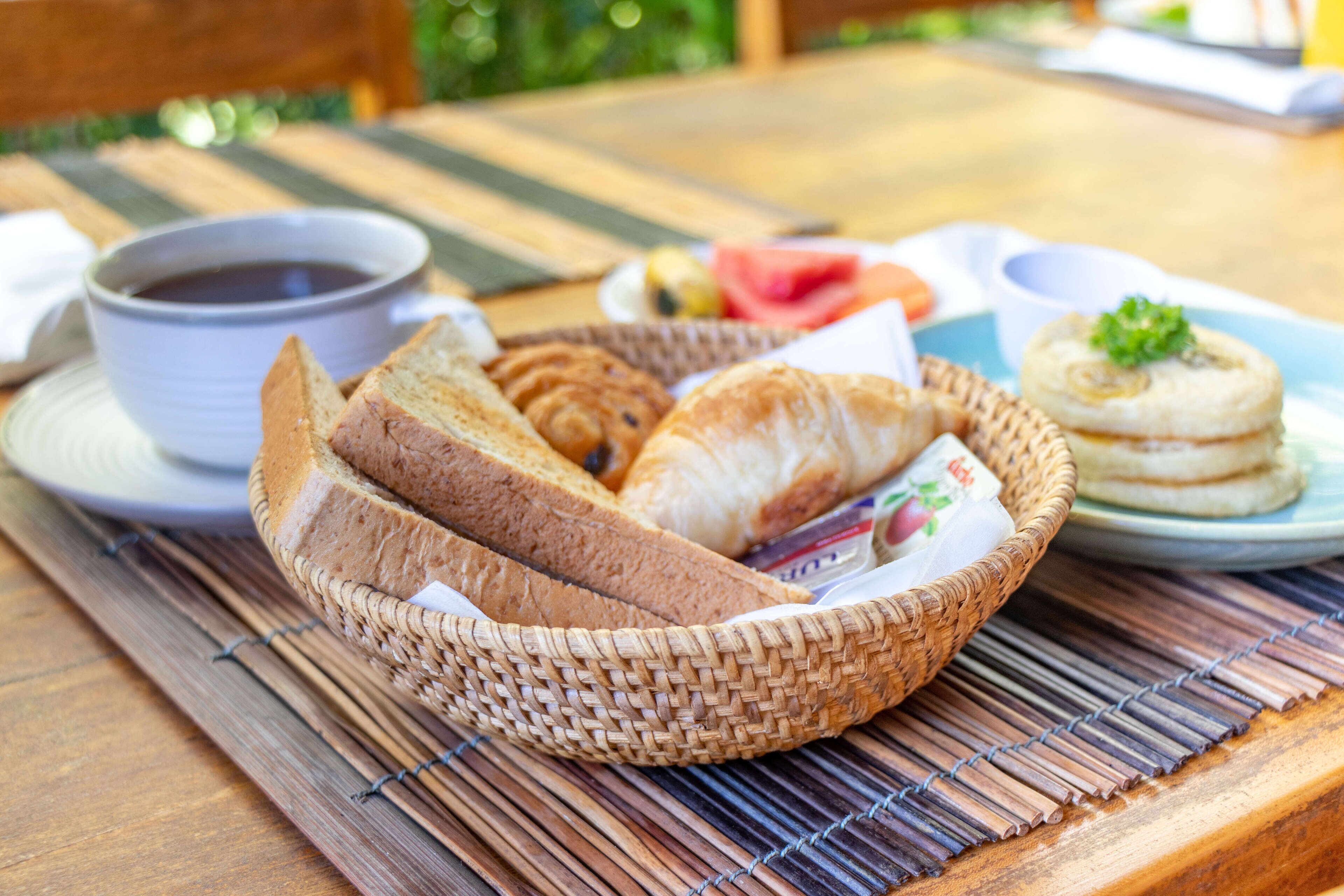 Un panier en osier contenant du pain et une assiette avec une pâtisserie, le tout posé sur une table en bois.