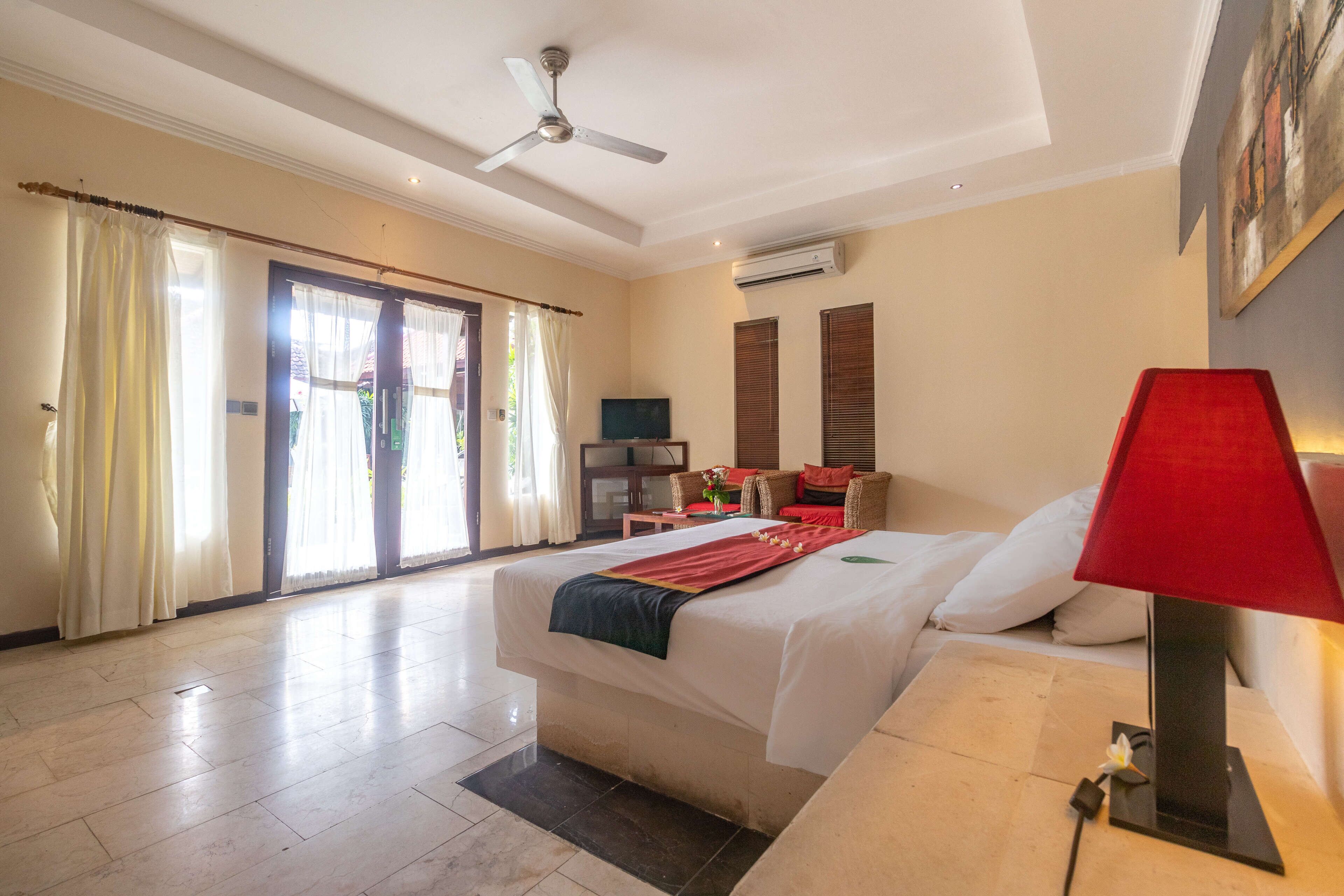 A hotel room with a bed, a red lamp, a ceiling fan, and a TV.