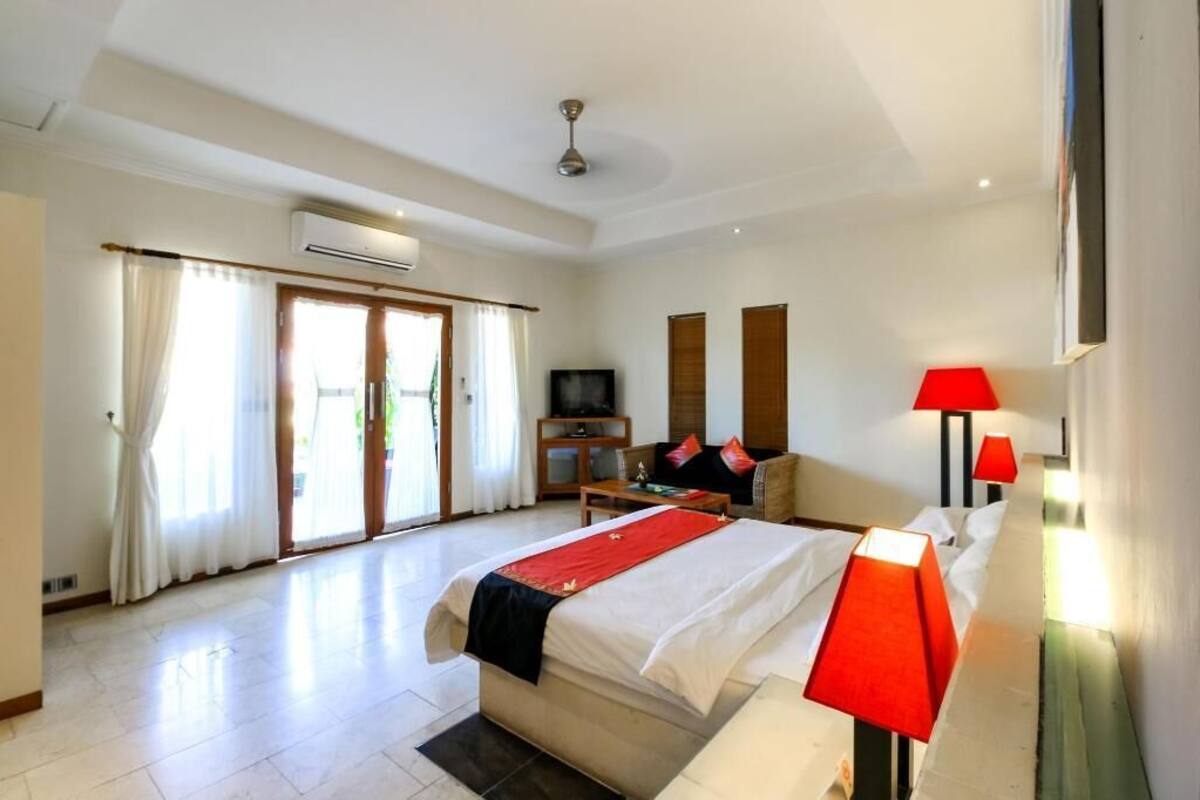 A hotel room with a bed, a TV, a desk, and a red lamp.