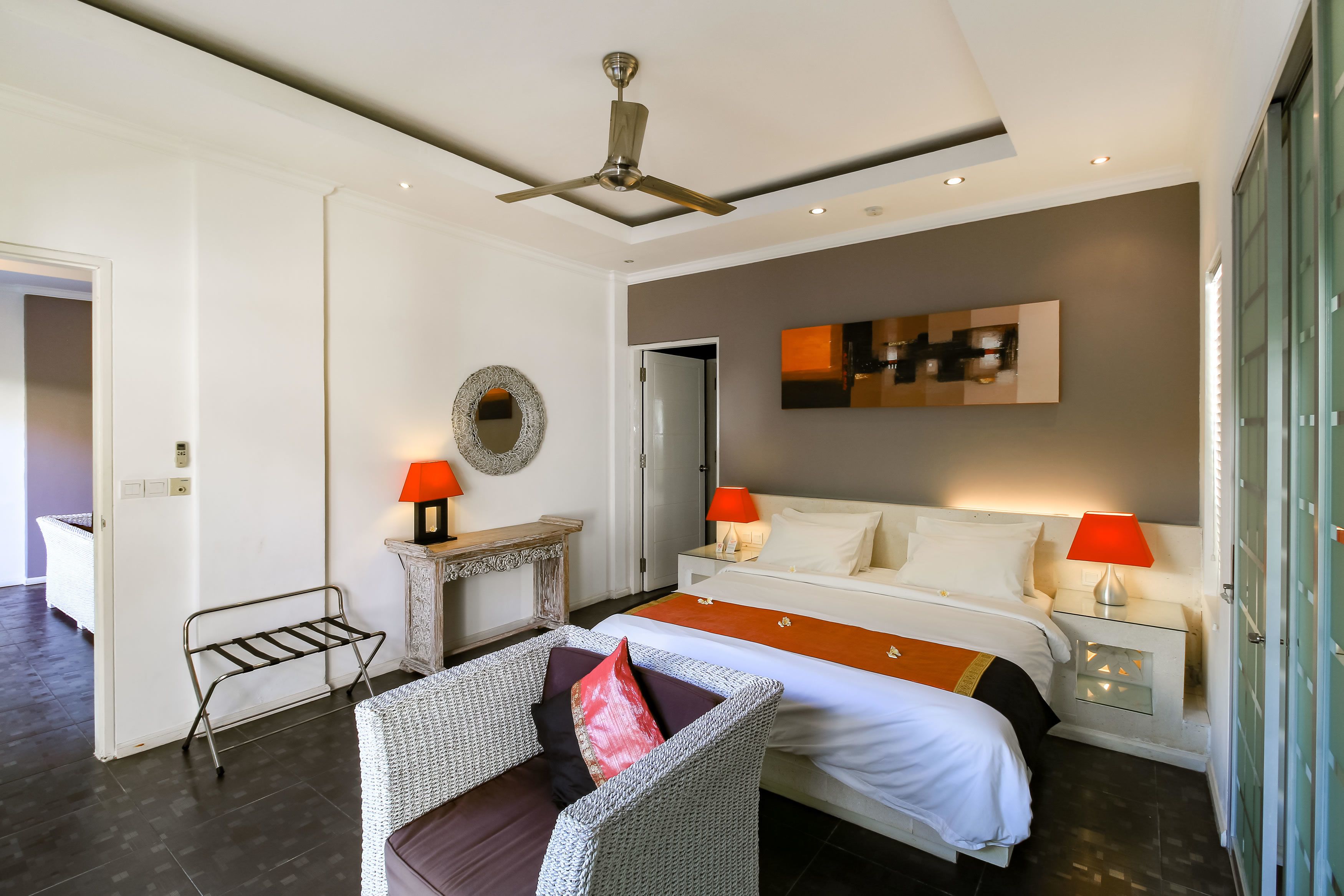 A modern hotel room with a bed, two bedside tables with lamps, a small side table, a mirror, and a ceiling fan.
