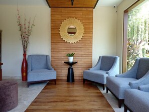 Una sala de estar moderna con dos sillones grises, un panel de pared de madera, un espejo redondo y una mesita con una planta.