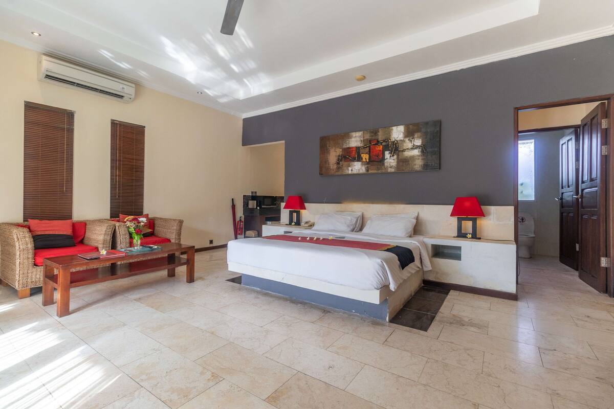 A spacious room with a large bed, a sofa, a coffee table, and a painting on the wall.
