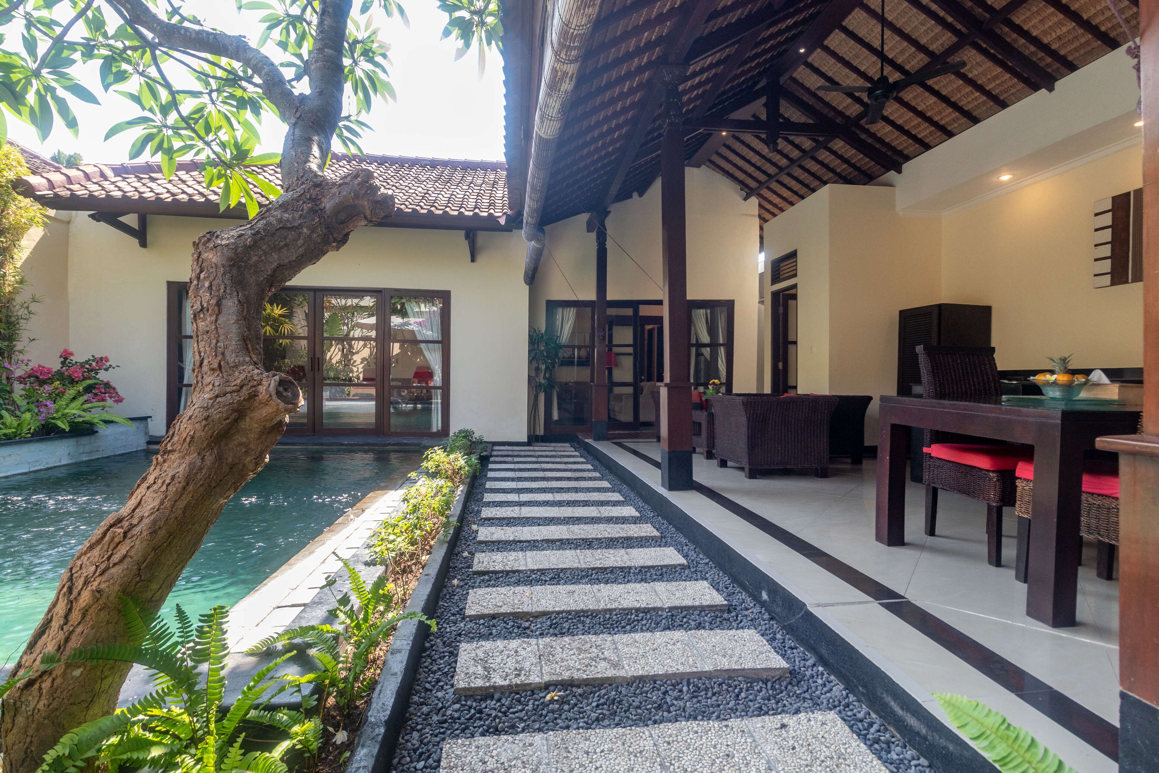 A pool area with a stone pathway, outdoor seating, and a pergola.